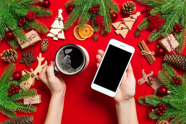 Vista superior de uma mulher segurando um telefone em uma mão e uma xícara de café na outra mão. Decorações de Natal e brinquedos.