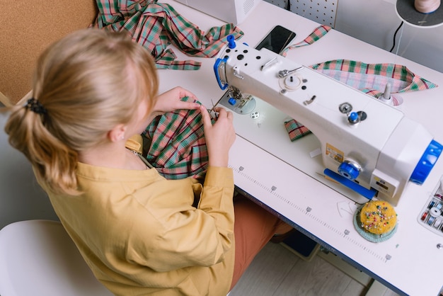 Vista superior de uma mulher trabalhando com uma máquina de costura em sua oficina, foco seletivo