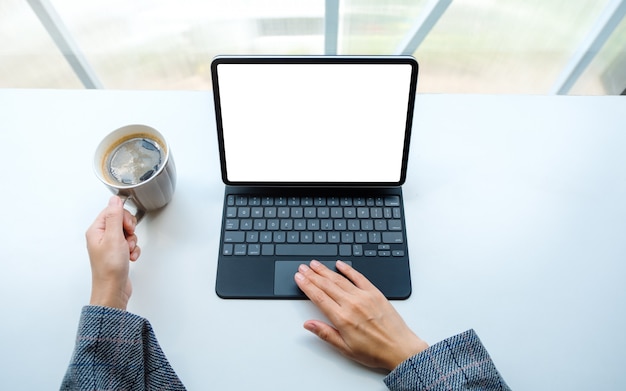 Vista superior de uma mulher usando e tocando no tablet touchpad com tela branca em branco como computador pc enquanto bebe café