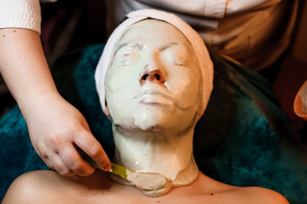 Vista superior de uma mulher Vista superior do rosto de uma mulher coberto pela máscara de alginato enquanto se inclina sobre uma cama de spa. rosto coberto por máscara de alginato enquanto se inclina sobre uma cama de spa.