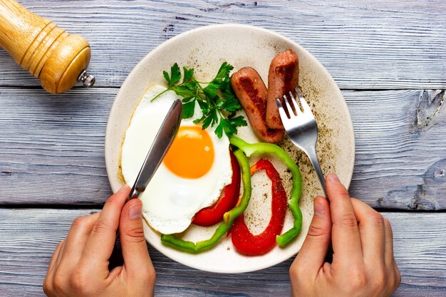 vista superior de uma pessoa comendo ovo frito com salsichas e vegetais em um prato