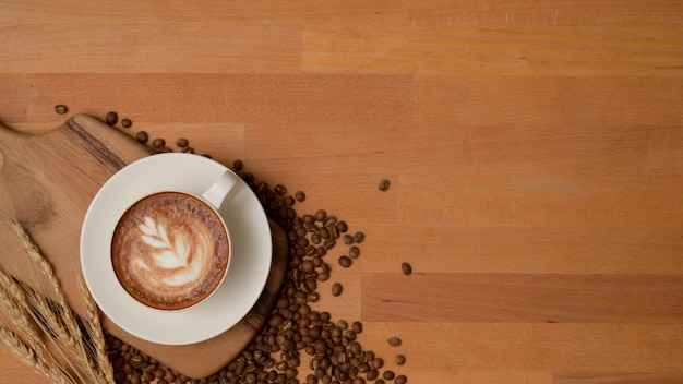 Vista superior de uma xícara de café com leite em uma mesa de madeira decorada com grãos de café, jogo americano e espaço de cópia