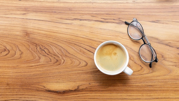 Vista superior de uma xícara de café de americano com óculos em fundo de madeira
