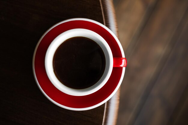 Foto vista superior de uma xícara vermelha de café preto em um prato na borda do espaço de cópia de mesa de madeira