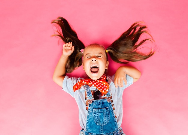 Vista superior debajo. Una niña extendió su cabello y se acuesta sobre un fondo rosa. concepto de niños.