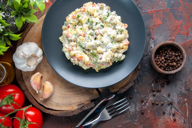 Vista superior deliciosa ensalada rusa dentro de la placa con tomates rojos frescos sobre una superficie oscura