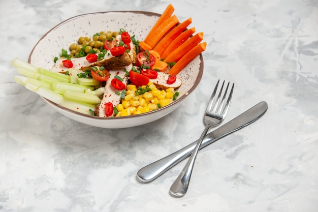 Vista superior de una deliciosa ensalada con varios ingredientes en un plato y cubiertos en superficie blanca