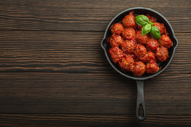 Vista superior de deliciosas albóndigas con salsa de tomate y albahaca fresca en sartén vintage rústico de hierro fundido servido sobre fondo de madera. Sabrosas albóndigas caseras con espacio para texto