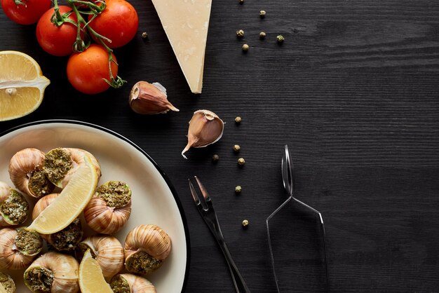 Foto vista superior de deliciosas caracoles cocidas con rebanadas de limón en una mesa de madera negra con ingredientes