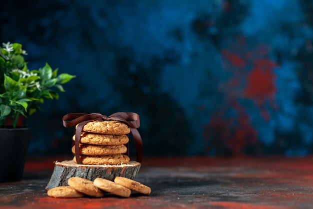 Vista superior de deliciosas galletas apiladas atadas con cinta sobre tabla de madera y maceta sobre fondo de colores mezcla oscuros
