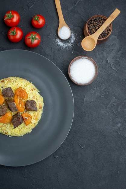 Vista superior delicioso arroz cocido pilaf con rodajas de carne y tomates en superficie oscura