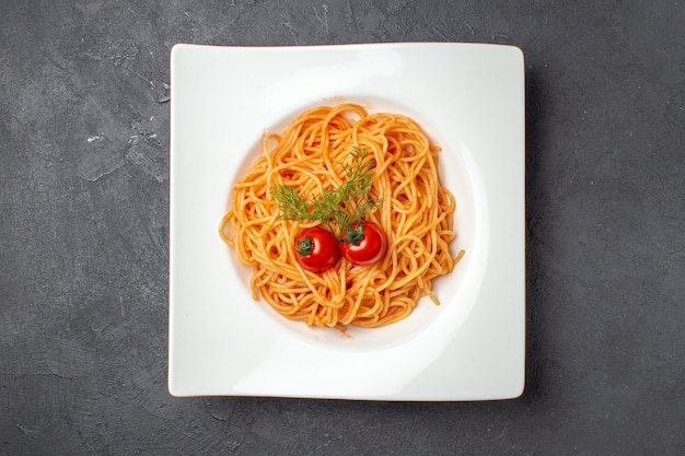 Vista superior de delicioso espagueti servido con tomates verdes en un plato de forma cuadrada blanca sobre fondo negro