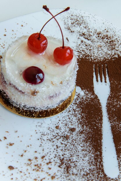 Vista superior del delicioso pastel de chocolate blanco con coco y cerezas en un plato y una decoración de cacao de contorno de horquilla