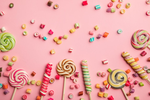 Vista superior de deliciosos dulces multicolores y piruletas sobre fondo rosa