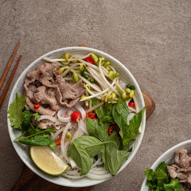 Vista superior de deliciosos fideos de carne vietnamita pho en un recipiente con ingredientes con espacio de copia.