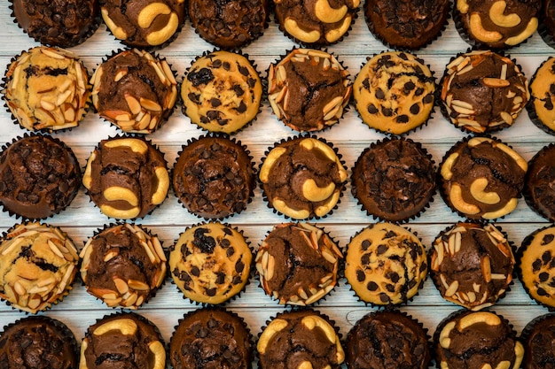 Foto vista superior de deliciosos muffins de vainilla y chocolate caseros frescos en un soporte para cupcakes de papel aislado sobre fondo de madera