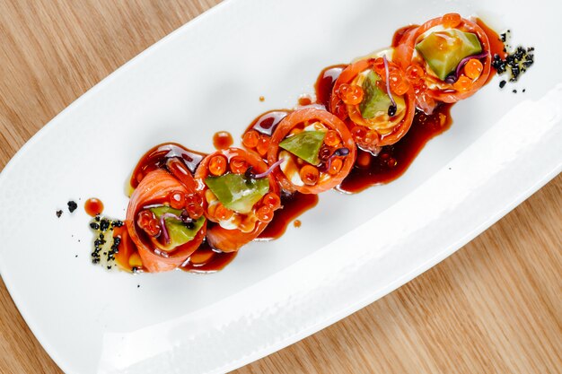 Vista superior de deliciosos rollos de salmón y aguacate con queso crema, caviar rojo en plato blanco. Comida sana en un restaurante.