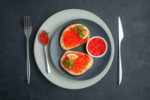 Vista superior deliciosos sándwiches de caviar dentro de la placa con tenedor y cuchillo sobre una superficie oscura