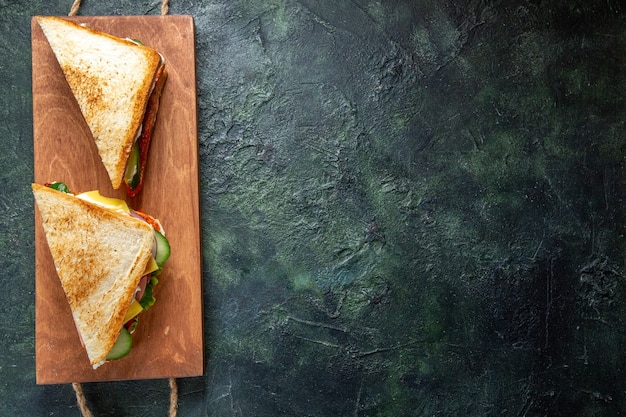 Vista superior deliciosos sándwiches de jamón en superficie oscura de tablero de madera