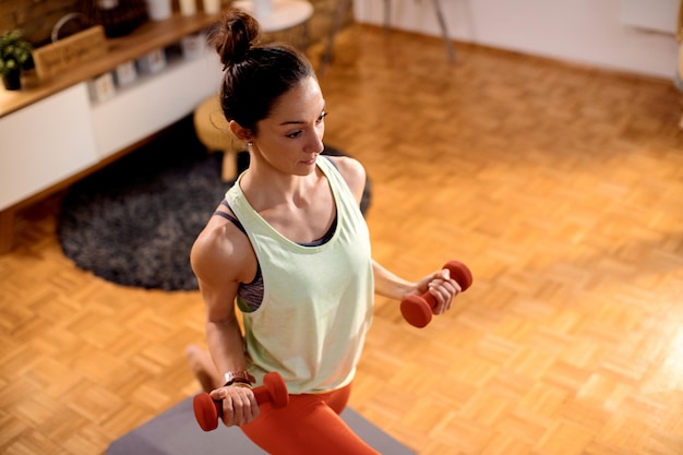 Vista superior de la deportista practicando estocadas mientras usa pesas de mano en casa