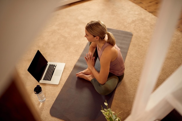 Vista superior de la deportista practicando Yoga mientras usa una computadora portátil en casa