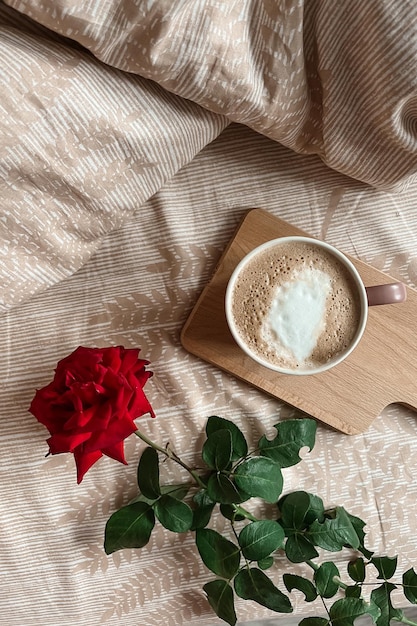 Vista superior del desayuno de la mañana en la cama con café capuchino en una bandeja y una flor de rosa roja Tarjeta de felicitación navideña