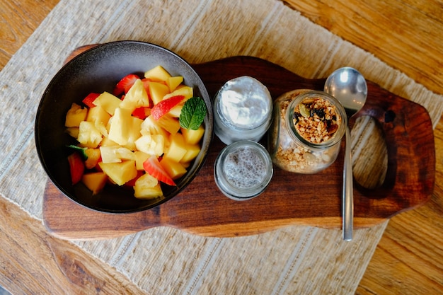 Vista superior de un desayuno saludable crudo con frutas tropicales, yogur, semillas de chía y granola