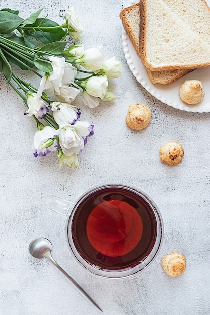 Vista superior de un desayuno con una taza de té, galletas, pan y flores.