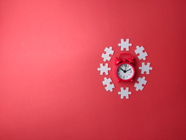 Vista superior despertador rojo con rompecabezas blanco sobre un fondo rojo