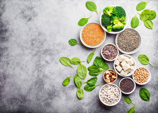 Vista superior de diferentes fuentes de proteínas veganas con espacio para texto: frijoles, lentejas, quinua, tofu, verduras, nueces, garbanzos, arroz, fondo de piedra. Nutrición vegetariana sana y equilibrada para veganos