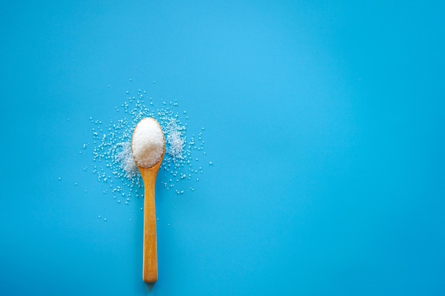 Vista superior do açúcar branco na colher de pau sobre fundo azul com espaço de cópia