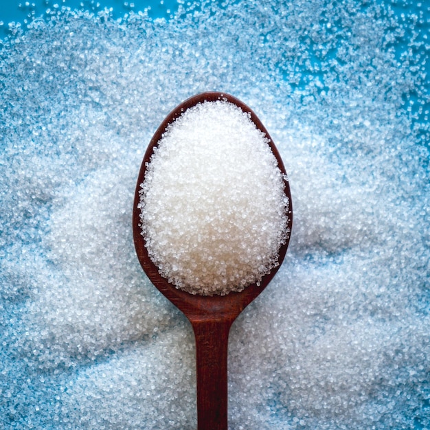 Foto vista superior do açúcar branco na colher de pau sobre fundo azul
