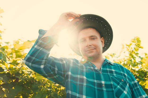 Foto vista superior do agricultor masculino vinificado olhando para a câmera em jovem vinhedo masculino com chapéu em um verão ensolarado.