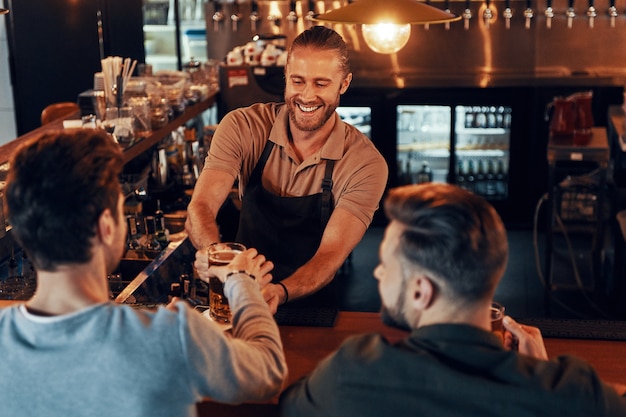 Vista superior do barman servindo cerveja para homens jovens em pé no balcão do bar em um pub