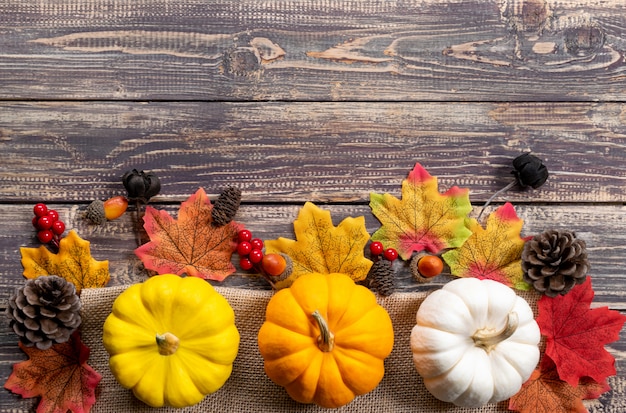 Vista superior do bordo de Outono folhas com abóbora e frutas vermelhas sobre fundo de madeira. Conceito de outono ou dia de ação de Graças.