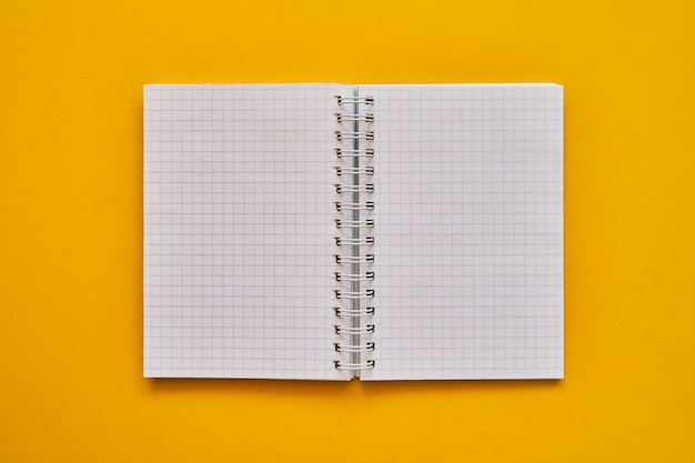 Vista superior do caderno aberto com páginas em branco. caderno escolar sobre um fundo amarelo, bloco de notas em espiral