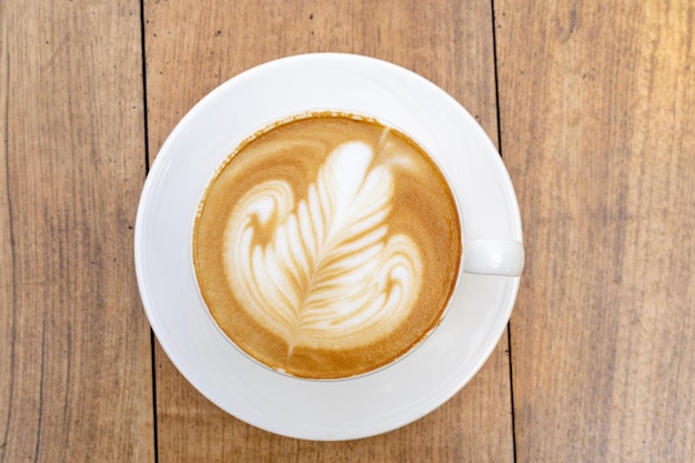 Vista superior do café com leite ou café cappuccino em xícara branca com bela arte de latte de árvore na mesa de madeira