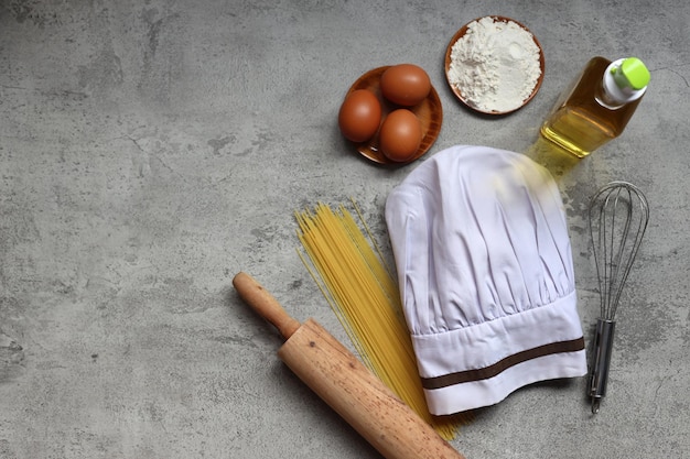 Vista superior do chapéu de chef com ingredientes e utensílios de cozinha em fundo rústico cinza