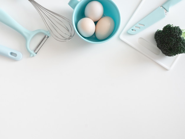 vista superior do conceito de sala cozinha com utensílios de cozinha, ovo e legumes no fundo da mesa branca.