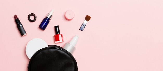Vista superior do conjunto de maquiagem e produtos para a pele derramando da bolsa de cosméticos na rosa