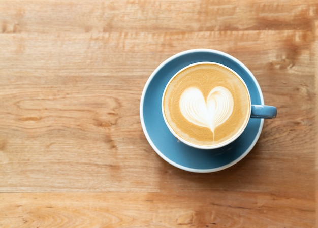 Vista superior do copo de café quente com uma espuma da forma do coração da arte do barista no fundo de madeira da tabela.