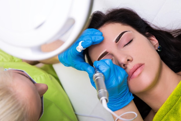Vista superior do cosmetologista aplicando maquiagem permanente nas sobrancelhas femininas