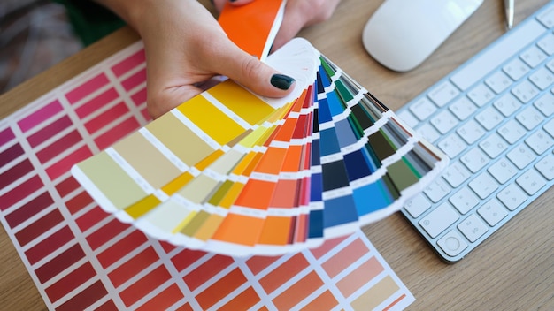 Vista superior do designer de mulher segurando o leque de amostras coloridas no designer de mão procurando adequadamente