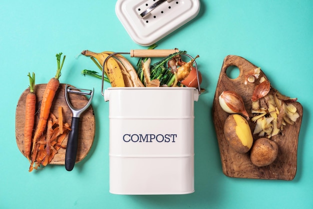 Vista superior do desperdício de comida da cozinha coletado na reciclagem de pote de compostagem Legumes descascados na tábua de cortar caixa de compostagem branca sobre fundo azul