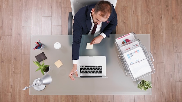 Vista superior do empresário colocando notas de stickey no laptop enquanto trabalhava nos investimentos da empresa