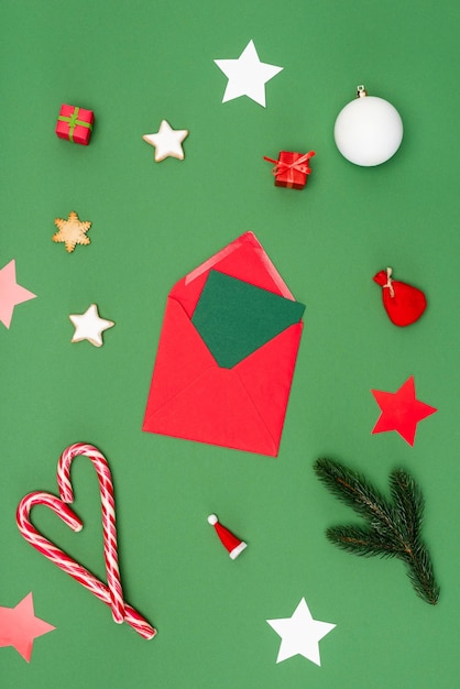 Vista superior do envelope vermelho com cartão perto de bolas de natal assadas estrelas e bastões de doces em verde