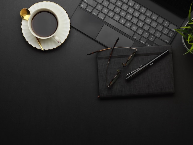 Vista superior do espaço de trabalho com xícara de café, suprimentos e laptop na mesa preta na sala de home office