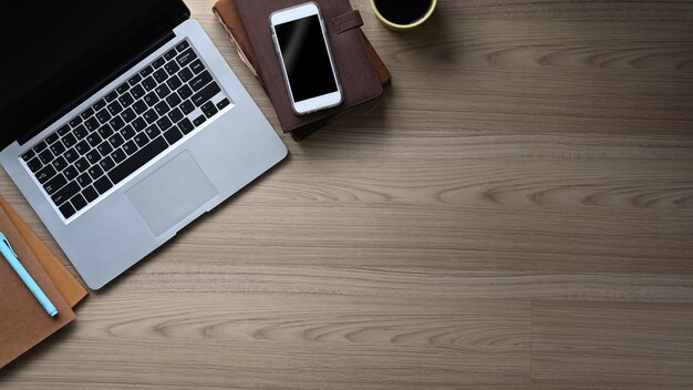 Vista superior do espaço de trabalho elegante com laptop, telefone inteligente, xícara de café, caderno e cópia espaço na mesa de madeira.