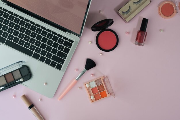 Vista superior do espaço de trabalho feminino com laptop e cosméticos em fundo rosa