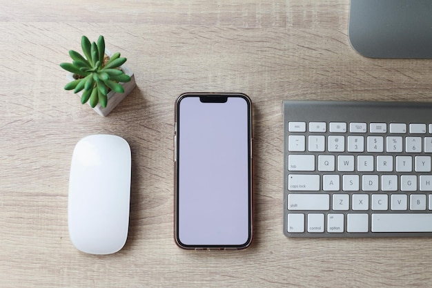 Vista superior do espaço de trabalho mínimo com smartphone de tela em branco, teclado laptop na mesa de escritório de madeira